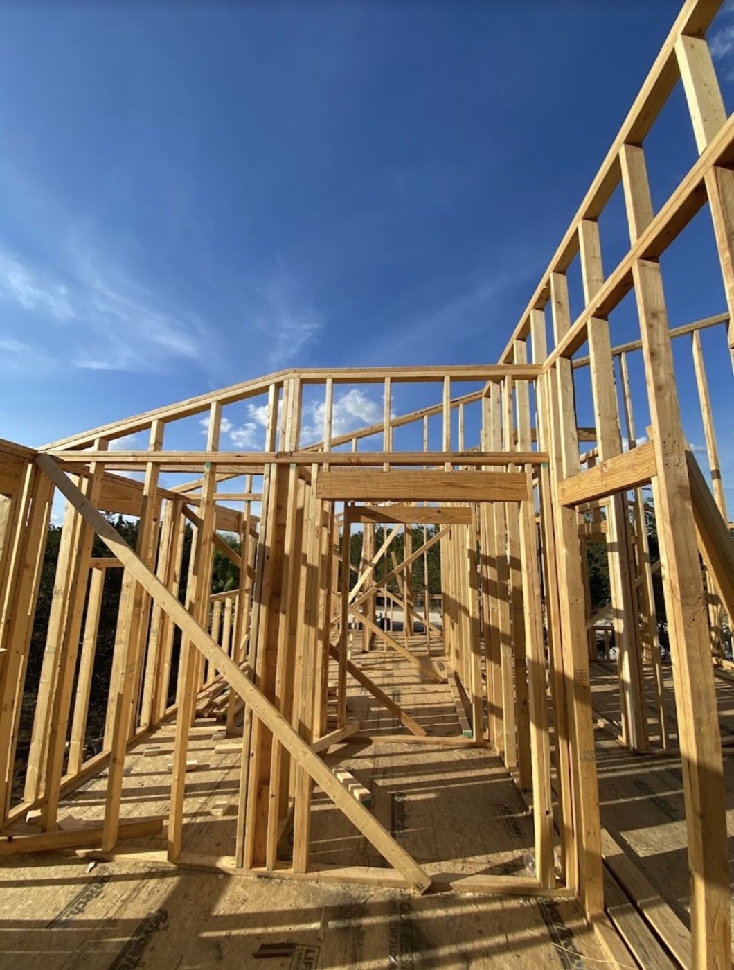 Wood-framed walls going up on a job site under a blue sky